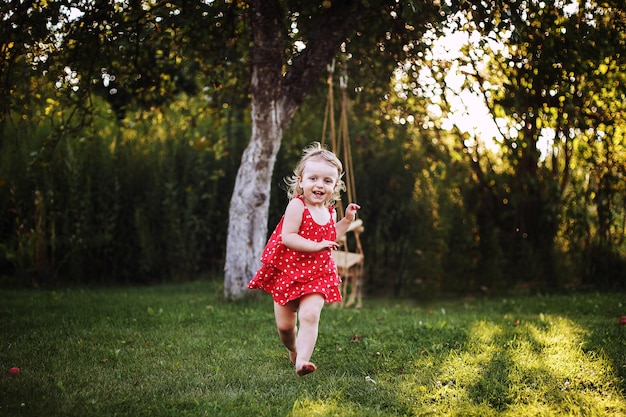 Gelukkige baby lacht een klein meisje dat in de tuin loopt bij zonsondergang buiten op blote voeten