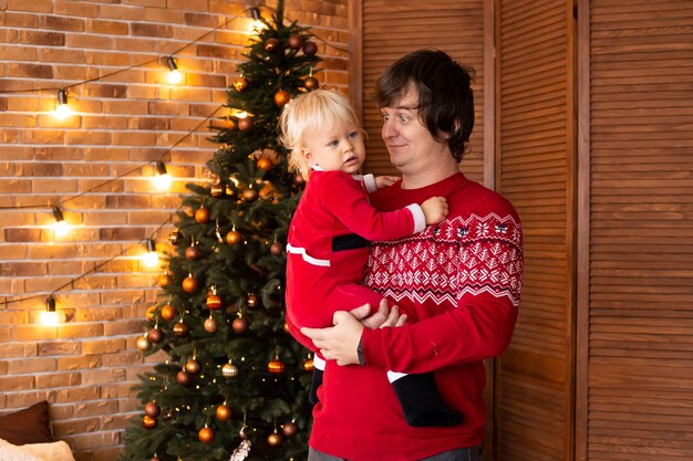 Gelukkige babyjongen en vader in feestelijk versierde kamer voor Kerstmis