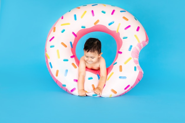 Gelukkige babyjongen in zwempak met zwemmende ringdoughnut op een gekleurde blauwe muur