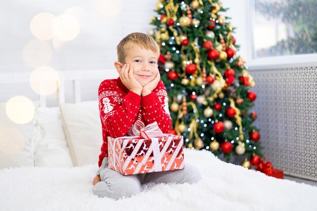 Gelukkige babyjongen is blij met cadeaus, de kinderen zijn thuis voor de kerstvakantie. Nieuwjaarsvakantie. Het kind zit in een feestelijk versierde kamer met een kerstboom. Portret van een kind