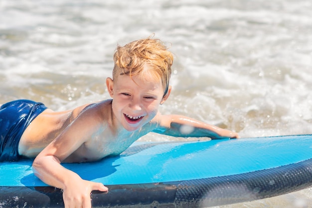 Gelukkige babyjongen - jonge surfer rit op surfplank met plezier op zee golven. Actieve gezinslevensstijl, buitenwatersportlessen voor kinderen en zwemactiviteit in surfkamp. Zomervakantie met kind