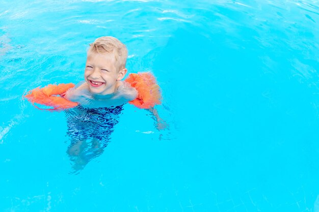 Gelukkige babyjongen zwemt of leert zwemmen in het blauwe waterzwembad in armbanden, het concept van zomervakanties en schoolvakanties