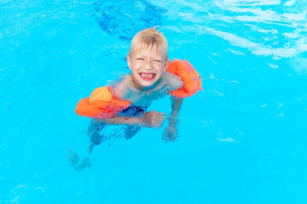 Gelukkige babyjongen zwemt of leert zwemmen in het blauwe waterzwembad in armbanden het concept van zomervakanties en schoolvakanties