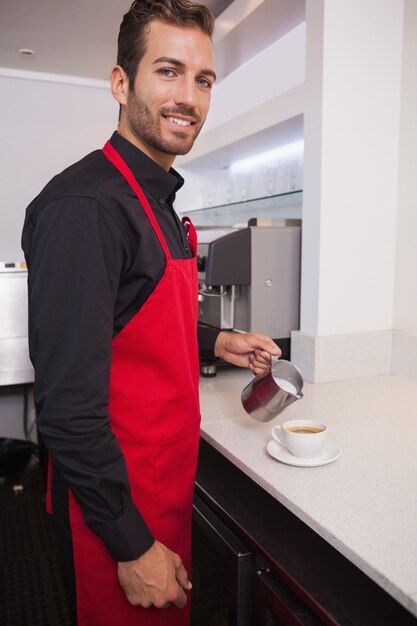 Gelukkige barista gietende melk in kop van koffie