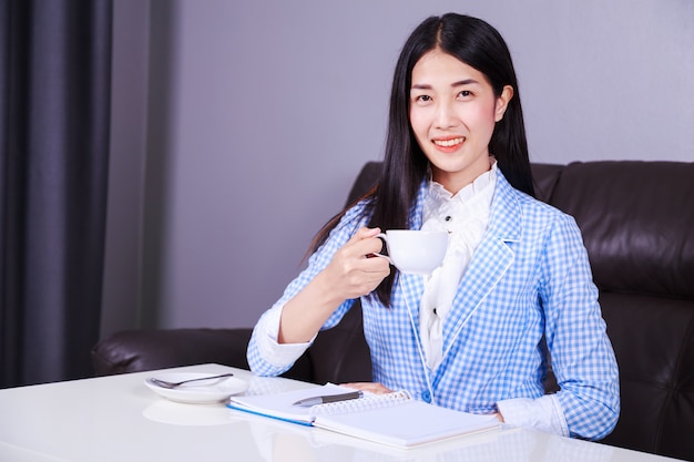 gelukkige bedrijfsvrouw die en een kop van koffie werkt drinkt