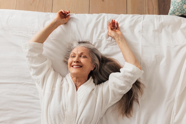 Gelukkige bejaarde vrouw in een badjas liggend op een bed met gesloten ogenx9xA