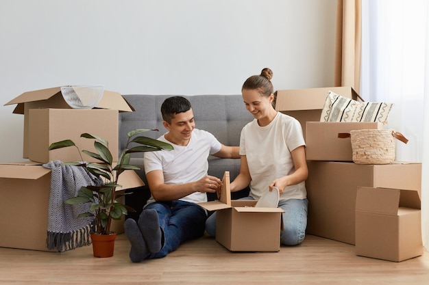 Gelukkige blanke familie verhuisde naar een nieuw appartement zittend op de vloer tussen kartonnen dozen verliefd paar huur een huis samen verhuisd in een nieuw huis persoonlijke bezittingen uitpakken