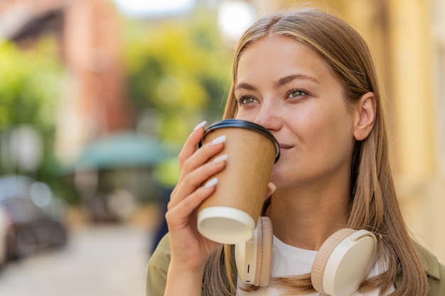Gelukkige blanke jonge vrouw die geniet van ochtendkoffie warm drankje en glimlachend op straat loopt