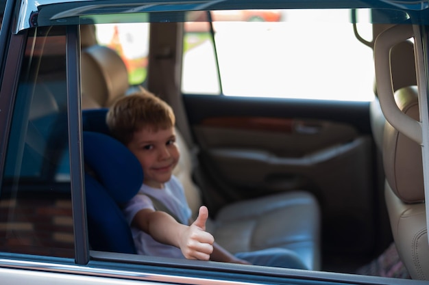 Gelukkige blanke jongen zittend in een blauw kinderzitje en duim tonend Reizend met een kind in een auto met een lederen interieur Portret van een schattige kleuter die een veiligheidsgordel draagt en klaar is om te rijden