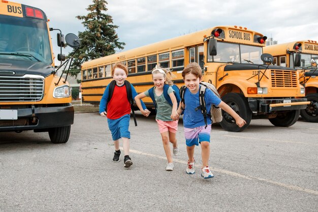 Foto gelukkige blanke kinderen jongens en meisjes kinderen studenten lopen in de buurt van gele schoolbus onderwijs