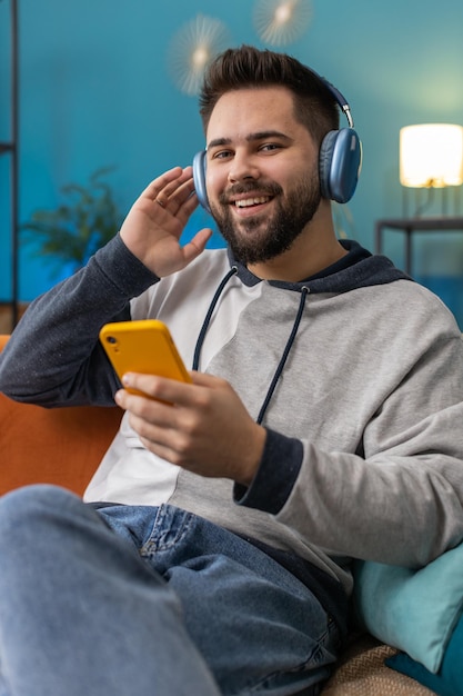 Gelukkige blanke man in draadloze koptelefoon ontspannen zittend op de bank thuis luisteren naar favoriete muziek