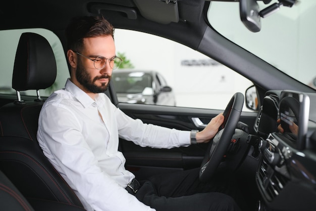 Gelukkige blanke man in formele kleding die in een luxe moderne auto stapt om het interieur te testen vóór aankoop Concept van verkoop en aankoop door een dealer