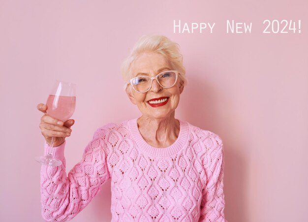 Foto gelukkige blanke oudere vrouw in cashmere roze trui drinkt roos op roze achtergrond viert