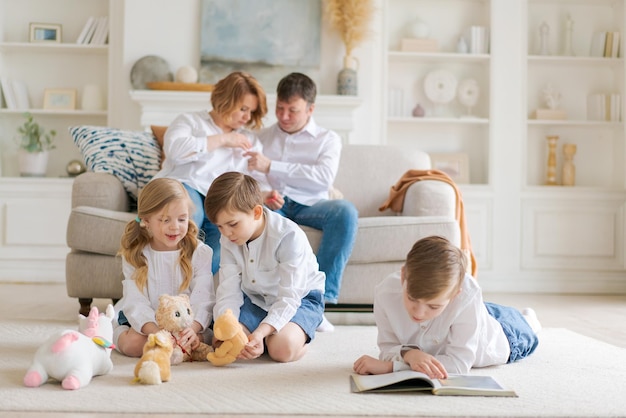 Gelukkige blanke ouders zitten ontspannen op de bank en kijken toe terwijl drukke kleine kinderen op de grond liggen en samen spelen, gezin met schoolkinderen ontspannen in de woonkamer, brengen het weekend thuis door