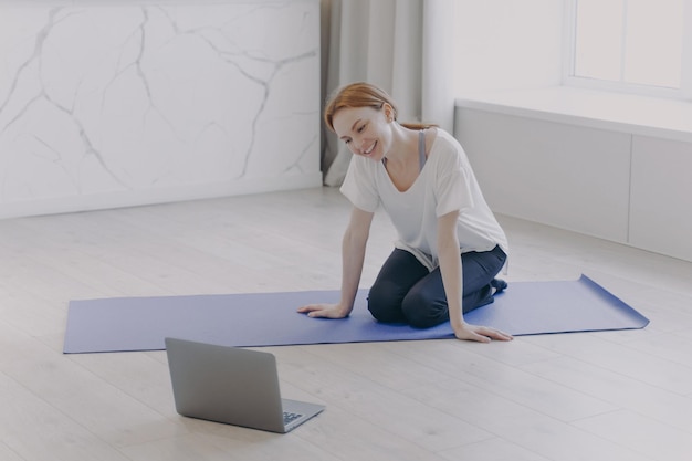 Gelukkige blanke vrouw heeft persoonlijke training op afstand voor de camera op yogamat op de vloer