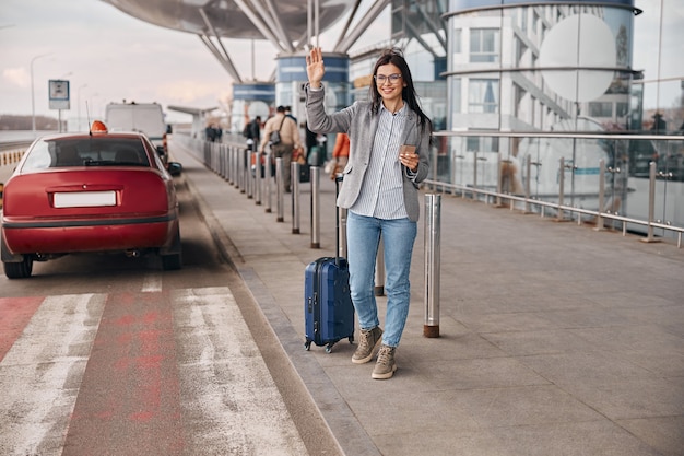 Gelukkige blanke vrouwenreiziger in de luchthaventerminal neemt een taxi