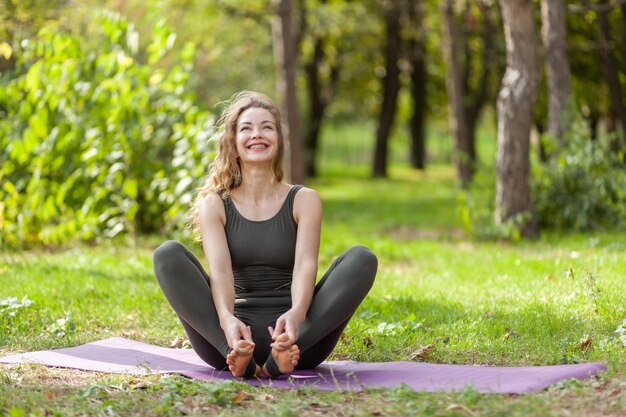 Gelukkige blanke yogi-vrouw zittend op een mat op het gras Gezonde levensstijl