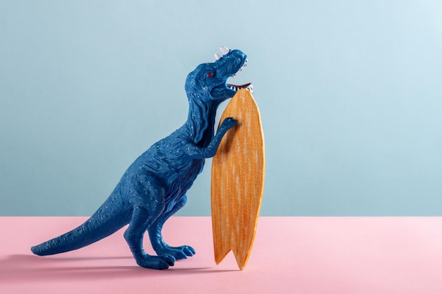 Foto gelukkige blauwe dinosaurus met houten surfplank op blauwe en roze achtergrond