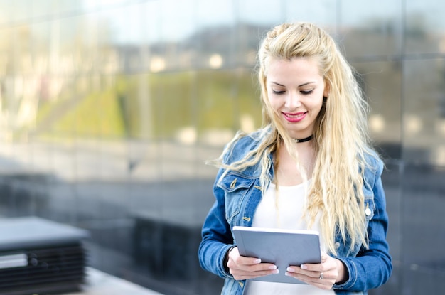 Gelukkige blonde student vrouw met tablet in een reflectie muur