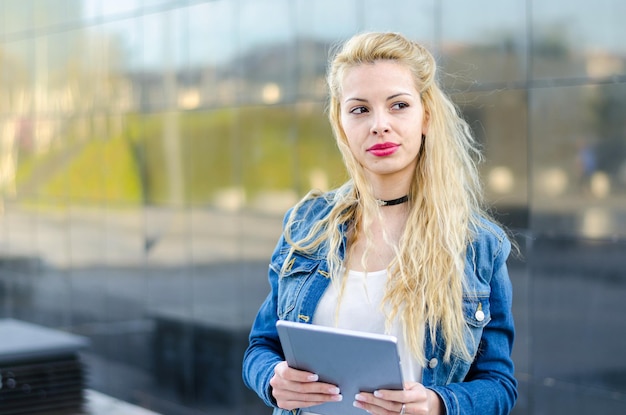 Gelukkige blonde studentenvrouw met tablet in een bezinningsmuur