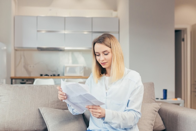 Gelukkige blonde vrouw die thuis op de bank zit, blij met tijdige betaling van kredietrekeningen en het sluiten van de kredietlijn, ontving goed nieuws van de bank