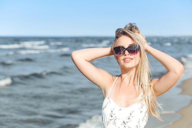 Gelukkige blonde vrouw in vrij geluk zaligheid op het oceaanstrand staand met een zonnebril en poseert