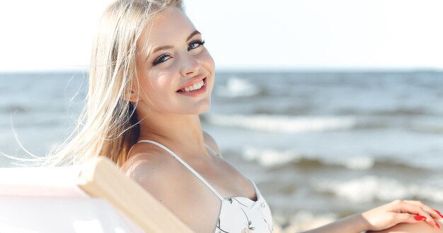 Gelukkige blonde vrouw ontspant zich op een houten leunstoel op het oceaanstrand