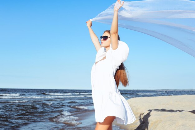 Gelukkige blonde vrouw vangt wolken en wind met haar armen op het oceaanstrand