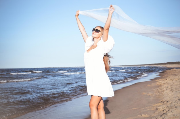 Gelukkige blonde vrouw vangt wolken en wind met haar armen op het oceaanstrand