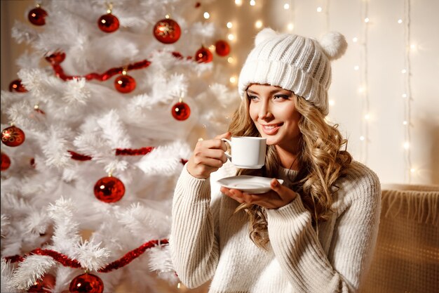 Gelukkige blondevrouw het drinken koffie, binnenlandse ruimte met Kerstmisdecoratie