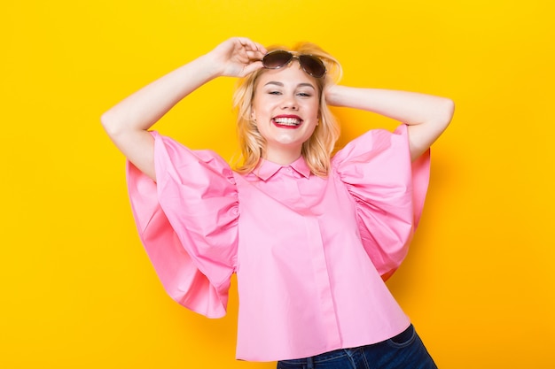 Gelukkige blondevrouw in roze blouse met zonnebril