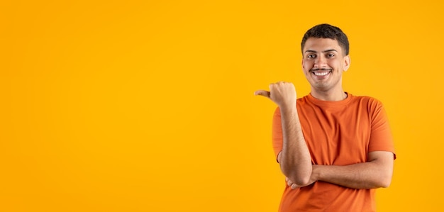 Foto gelukkige braziliaanse man die met zijn duim opzij wijst naar kopieerruimte en reclame maakt voor een geweldige aanbieding oranje