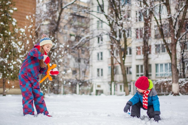 Gelukkige broer en zus spelen sneeuwballen tijdens een winterwandeling en maken sneeuwballen in het park