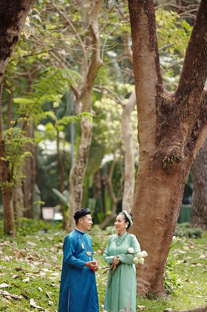 Gelukkige bruid en bruidegom in traditionele Vietnamese kostuums praten in park na huwelijksceremonie