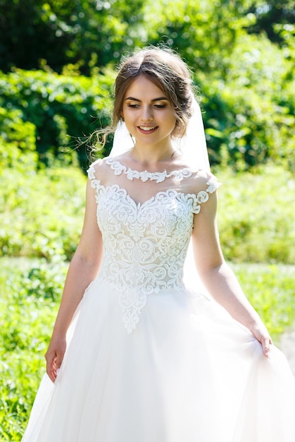 Gelukkige bruid in een lange witte trouwjurk en sluier in een groen park op de natuur. Bruiloft afbeelding van een jong meisje, vrouwen make-up en kapsel. huwelijk concept