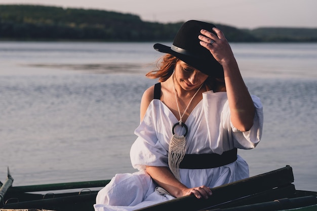 Gelukkige bruid in zwarte hoed in een boot op de rivier