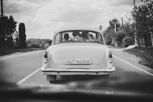 Foto gelukkige bruid kus bruidegom pasgetrouwde bruidspaar is het besturen van een retro auto op een landweg voor huwelijksreis na de ceremonie manier de beste dag en huwelijk net getrouwd zwart-wit foto