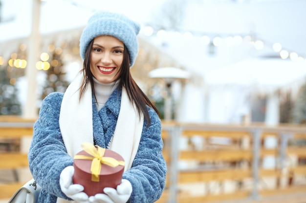 Gelukkige brunette vrouw in winterjas met een geschenkdoos op kerstmarkt. Ruimte voor tekst