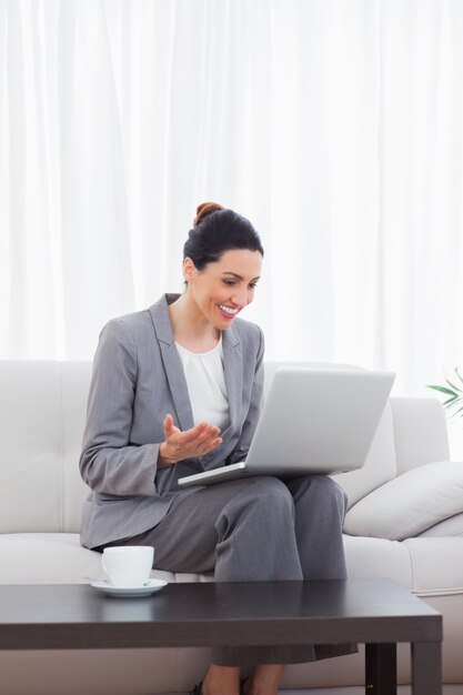 Gelukkige busineswomanzitting op bank die laptop met behulp van