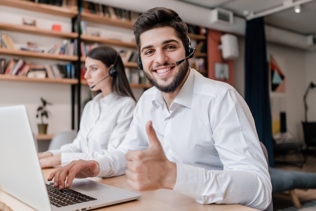 Gelukkige call centreexploitant die van het middenoosten en duimen in het bureau glimlachen tonen