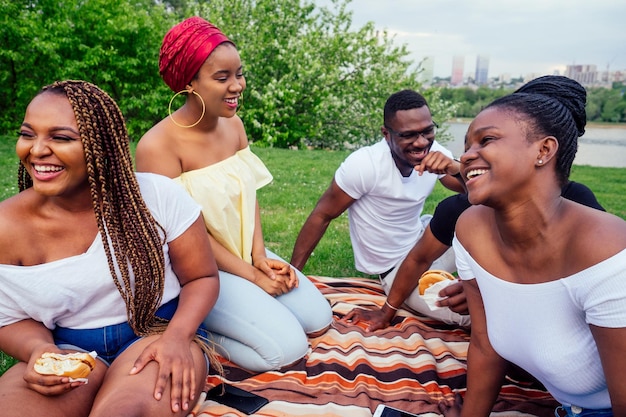 Gelukkige, casual amerikaanse afrikaanse mensen die plezier hebben en hamburgers eten buitenshuis lifestylestudenten voor een pauze zomeravond bewolkt weer in park