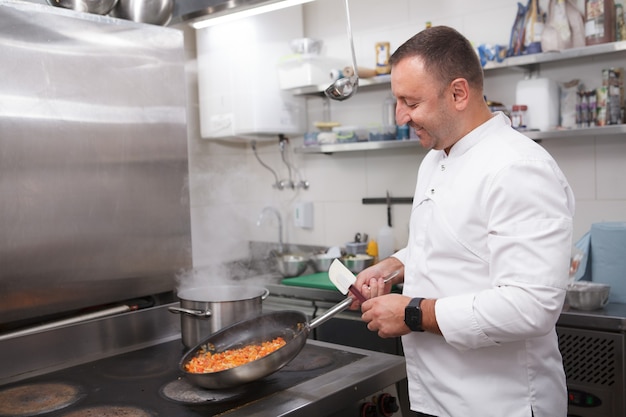 Foto gelukkige chef-kok die geniet van het werken in zijn restaurant, groenten frituren, ruimte kopiëren