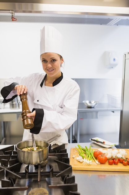 Gelukkige chef-kok die peper toevoegt aan soep