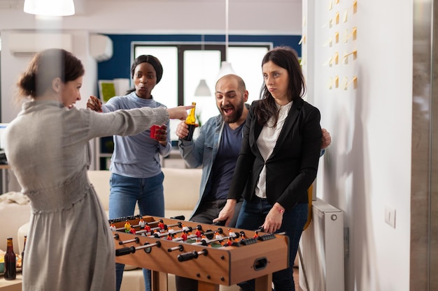 Gelukkige collega's die na werkuren tafelvoetbal spelen, bier drinken en pizza eten. Kantoorcollega's die vrijetijdsactiviteiten doen tijdens feestviering met snacks.