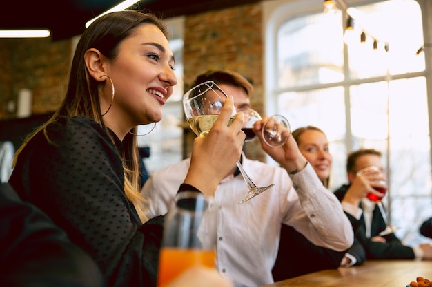 Gelukkige collega's vieren terwijl bedrijfsfeest, bedrijfsevenement. Jonge blanke mensen in zakelijke kleding praten, wijn drinken. Concept van kantoorcultuur, teamwork, vriendschap, vakantie, weekend.