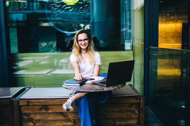 Gelukkige dame zit met laptop in cafetaria