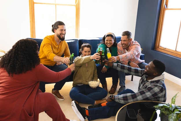 Foto gelukkige diverse mannelijke en vrouwelijke vrienden praten, eten popcorn en drinken bier thuis.