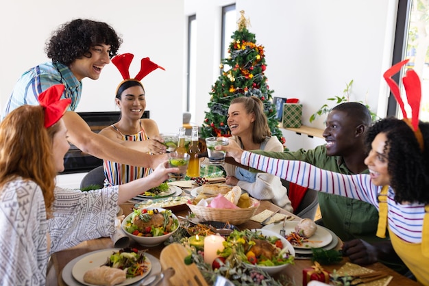 Gelukkige diverse vrienden die aan tafel zitten en dineren met Kerstmis