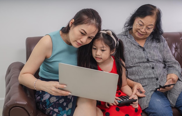 Gelukkige drie generaties vrouwen zitten ontspannen op de bank en kijken naar grappige video's op laptop