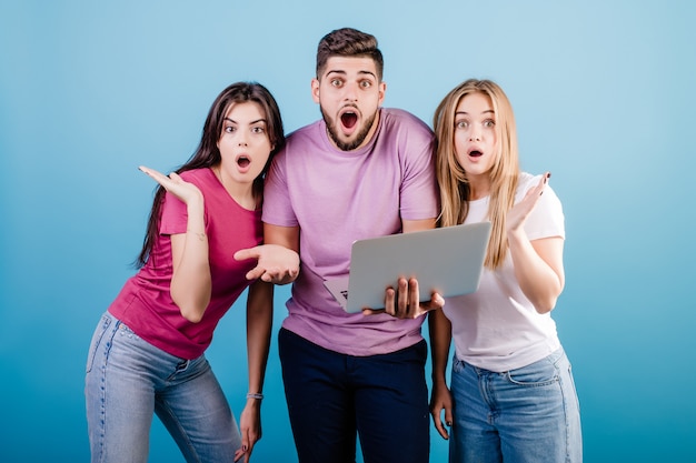 Gelukkige drie jonge vriendenman en vrouwen die laptop op blauw bekijken